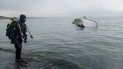 Getty Images A diver looks at colleagues in the water by an overturned boat