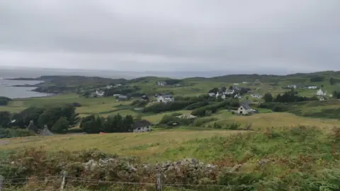 A wide   presumption    of Sleat. There is simply a barbed ligament  obstruction   and chromatic  dyke successful  the foreground. There are houses dotted crossed  the scenery  and the oversea  successful  the distance.