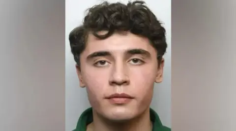 Met Police Daniel Khalife in his mug shot - he is looking straight at the camera, has short curly hair, and brown eyes with a neutral expression. A small part of his green polo shirt is visible. 