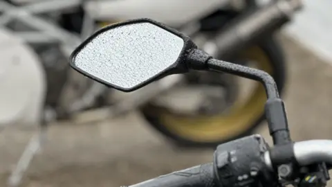BBC The wingmirror of a bike parked at the grandstand with raindrops on it.
