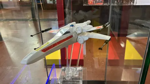 Close up view of an x wing plane from the Star Wars film in a museum display cabinet.