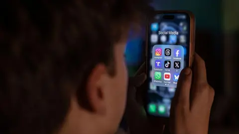 A boy looks at a phone with social media apps open.