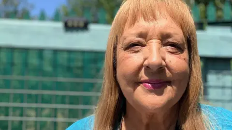 Linda, a woman with shoulder-length golden hair, wearing a blue top, smiling for the camera.