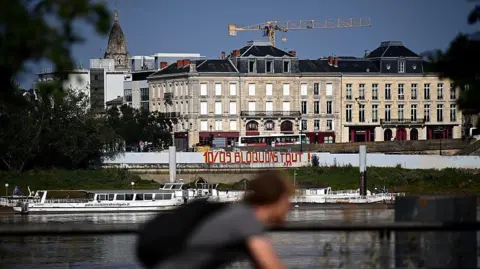 AFP via Getty Images A cyclist pedals past graffiti reading 'September 10 Let's block everything' on the wall of a construction site on a river in Bordeaux
