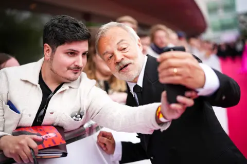 Getty Images Graham Norton taking a selfie with a fan behind a barrier