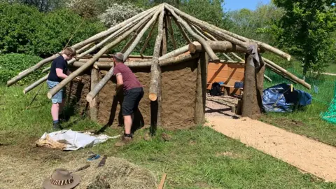 Operation Phoenix Two people fix logs to create the roof structure of the Iron Age-style roundhouse