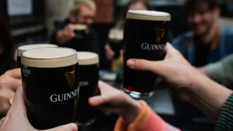 A crowd of people holding Guinness pints in a cheers motion.