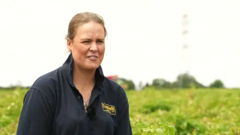 Polly Megginson pictured in a farmer's field. She has fair-coloured hair and is wearing a blue polo shirt.