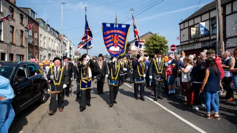 Royal Black Institution Members of the Royal Black Institution marching through a street in Ballymena, with members of the public standing on either side of the road.