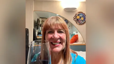 Mary Ann Demsar Woman smiles as she holds glass of red wine in cabin.