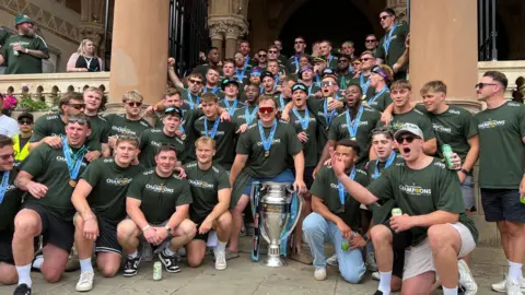 The squad, all wearing green t-shirts and gold medals, posing for a group picture.