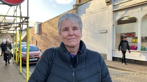 Emily Coady-Stemp/BBC Lisa Payne looks at the camera. She has short grey hair and is wearing a black coat.