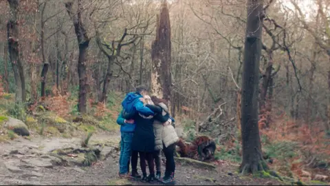 Docsville Studios, gives a group of people who wear a group jackets of each other in a wooded area.