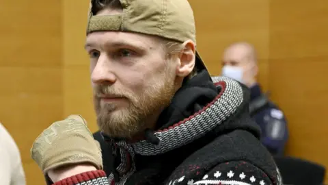 Voislav Torden appears in court in Helsinki, wearing a patterned hoodie, and khaki gloves and baseball cap.