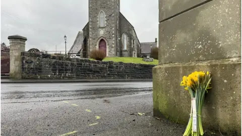 Flowers propped against a wall on the Boa island Road