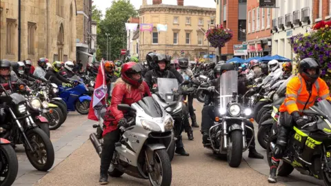 Scores of bikers are sat on their motorbikes wearing helmets and ready to set off from Gloucester city centre.
