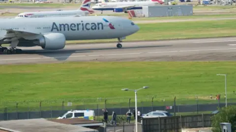Heathrow Airport scene - a police vehicle and protestors can be seen airside 