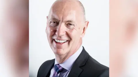 The Dark Money Files A company head and shoulders portrait photo of Mr Barrow who is smiling at the camera against a white background
