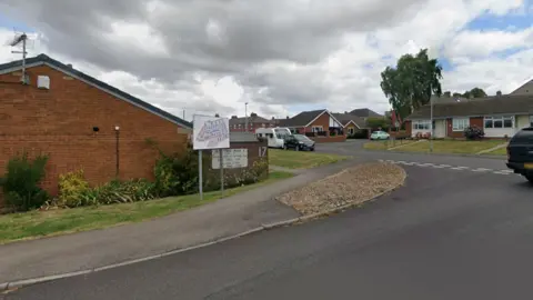 A quiet housing estate with cars parked along the sides of the road
