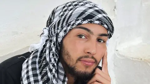 Nottinghamshire Police Marley Gascoine wearing a black and white head scarf Keffiyeh. He has a short dark beard as well.