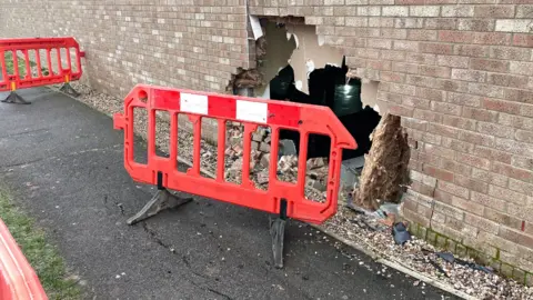 A red plastic gate is pictured in front of a brick building, with a large hole in the middle.