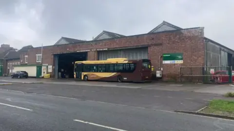 Daniel Mumby A tired looking depot with a brown and yellow bus parked outside