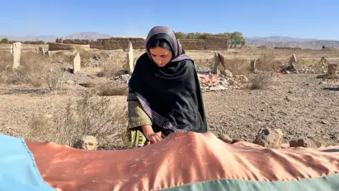 BBC/Farhat Javed Mahrang kneels at her father's grave in a black shawl