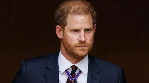 EPA An image of Prince Harry, who has short red hair and facial hair, wearing a blue suit jacket, white shirt and dark red tie against a dark brown background. He has a neutral expression.