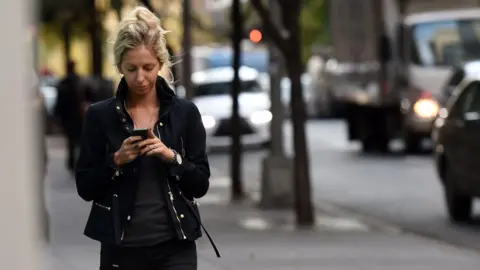 Getty Images A woman uses her smartphone as she walks in New York, 13 November 2014