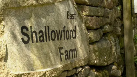 A close up of the sign for East Shallowford Farm on a traditional stone wall.