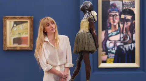 PA Media A woman in a gallery looks at a statue of a young ballet dancer. 