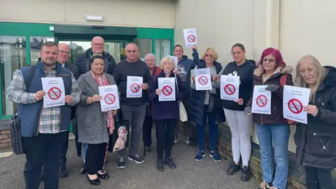 Terry Jermy office Terry Jermy with a group of people outside a council building all holding signs which have a no entry sign printed on them.