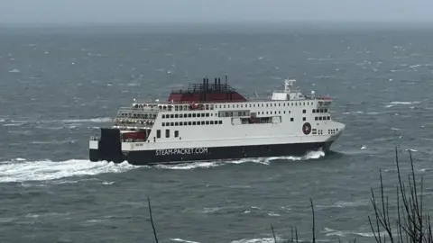 BBC The Manxman, which is a large ferry in white black and res with Steam-Packet.com on the side, sailing through choppy seas in Douglas Bay.