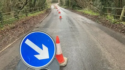 Local Democracy Reporting Service A line of red and white bollards and a blue and white keep right sign stretch down a deserted country road and into the distance.
