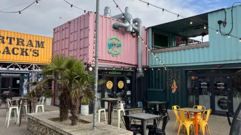Jon Wright/BBC Beach Street in Felixstowe with brightly coloured shipping containers as with glass doors and cafe seating in front.