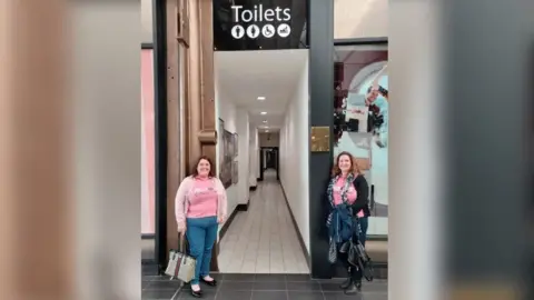 Mums on a Mission Mums on a Mission's Louise and Jessica outside the accessible toilet at the MacArthur Glen designer outlet in Redbourne, Swindon. They are weating pink Mums on a Mission t shirts.