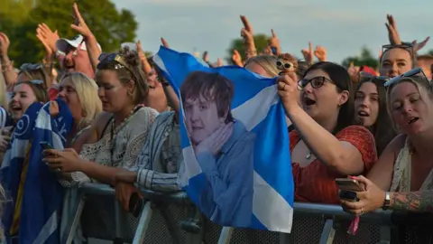 Getty Images Fans at a music festival watching Lewis Capaldi, including holding a Saltire with a picture of him on it.