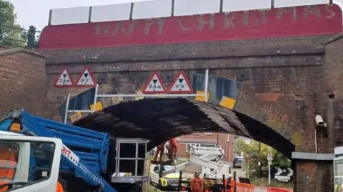 Nicky Coppins The Christmas Bridge being repainted by people in high vis clothing. They are standing on a platform being raised by a piece of machinery.