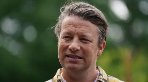 PA Media A man with mainly brown hair and a yellow, black and white top. The green background is blurred.