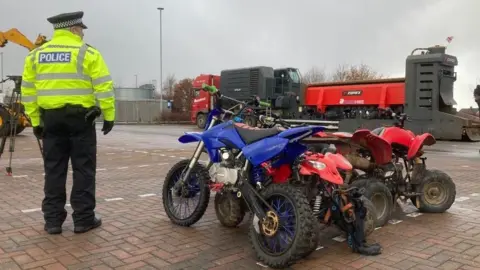 A police officer stood next to some off road bikes.