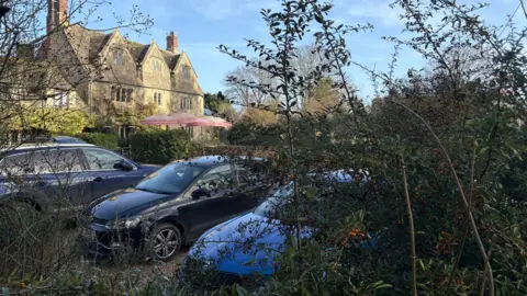 Cars parked outside a large cotswold stone pub.