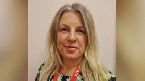 Julie Thomas has long blonde hair and is wearing makeup.