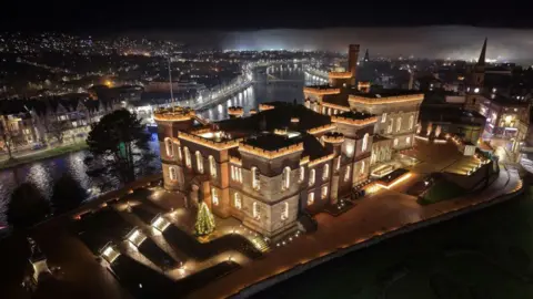 Gus MacLellan An aerial shot of the castle which is lit up against a dark night.