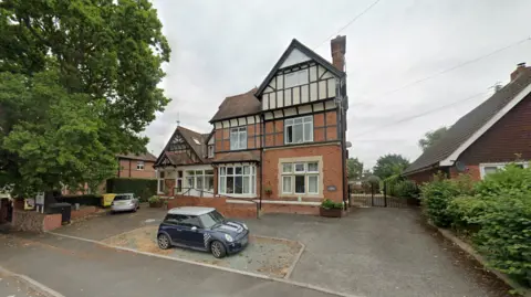 A three storey Edwardian house pictured with a blue Mini Cooper parked outside it. 