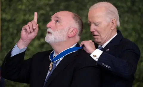 Getty Images Jose Andres point his index finger to the sky as Joe Biden wraps a medal around his neck