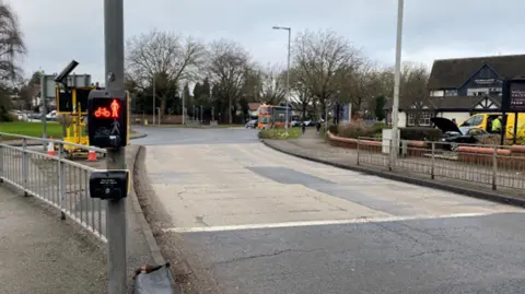 National Highways Priory Roundabout in Nottingham with a Miller and Carter restaurant to the right. At the front of the image there is a pedestrian crossing which is displaying a red light.