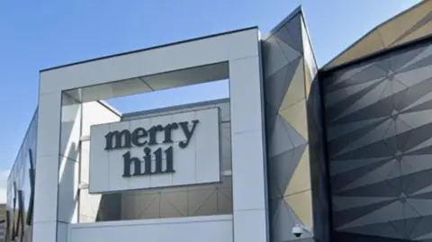 The modern frontage of a shopping centre, with the words Merry Hill set in a large suspended sign
