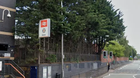 Google A sign showing Aston railway station by the side of a road