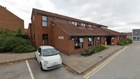 A GP practice building viewed from the car park