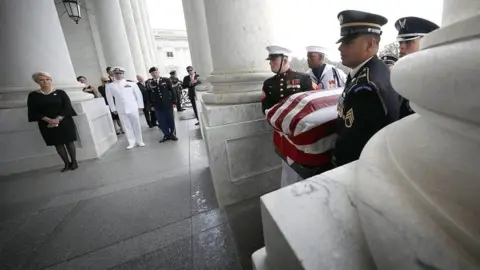 EPA John McCain's widow Cindy McCain and his sons Jack (C) and James (R) watch joint service members of a military casket team carry the casket of Senator John McCain into the US Capitol in Washington DC on 31 August 2018